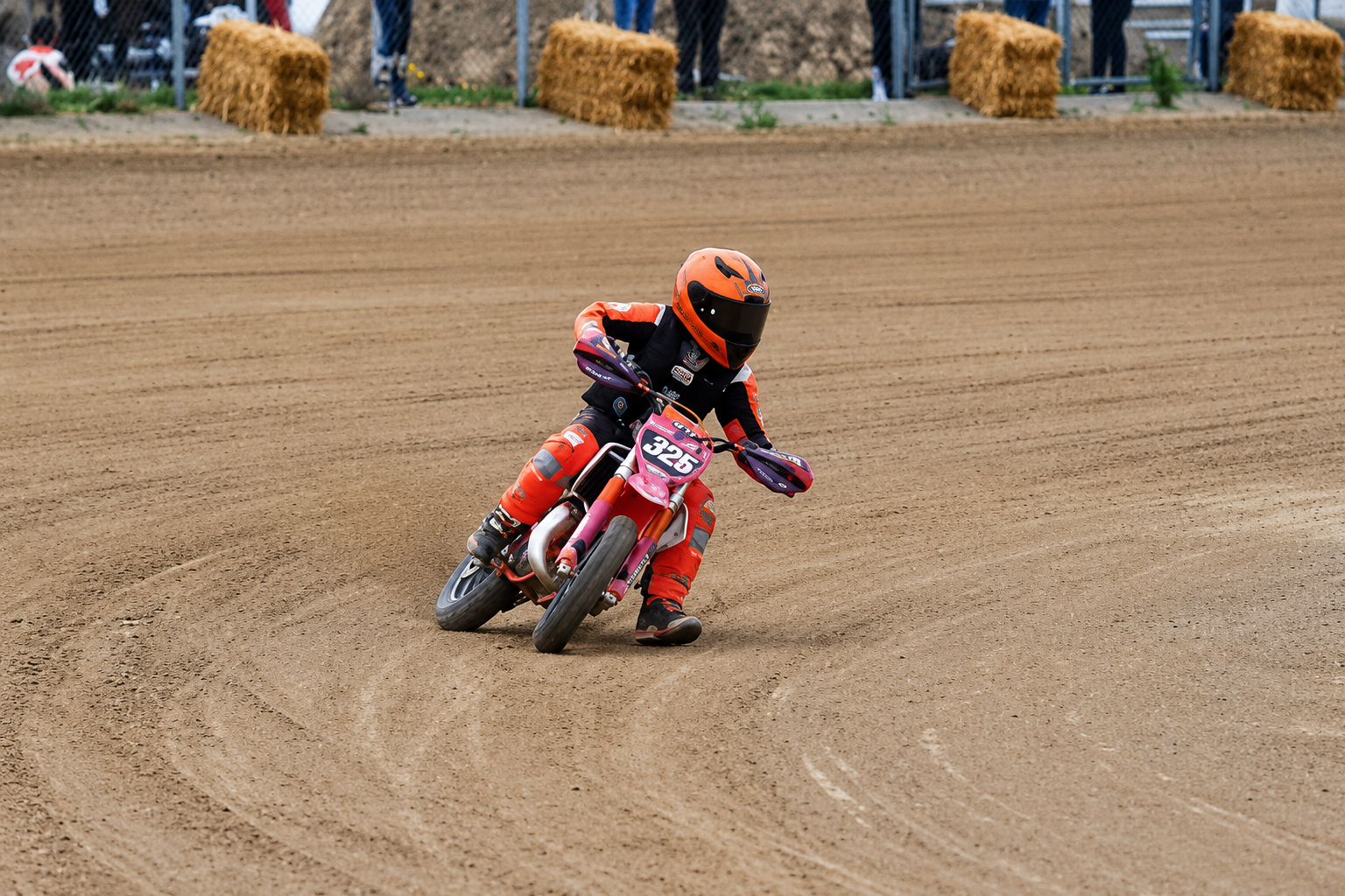 Child on a dirt bike racing on a dirt track with hay bales in the background