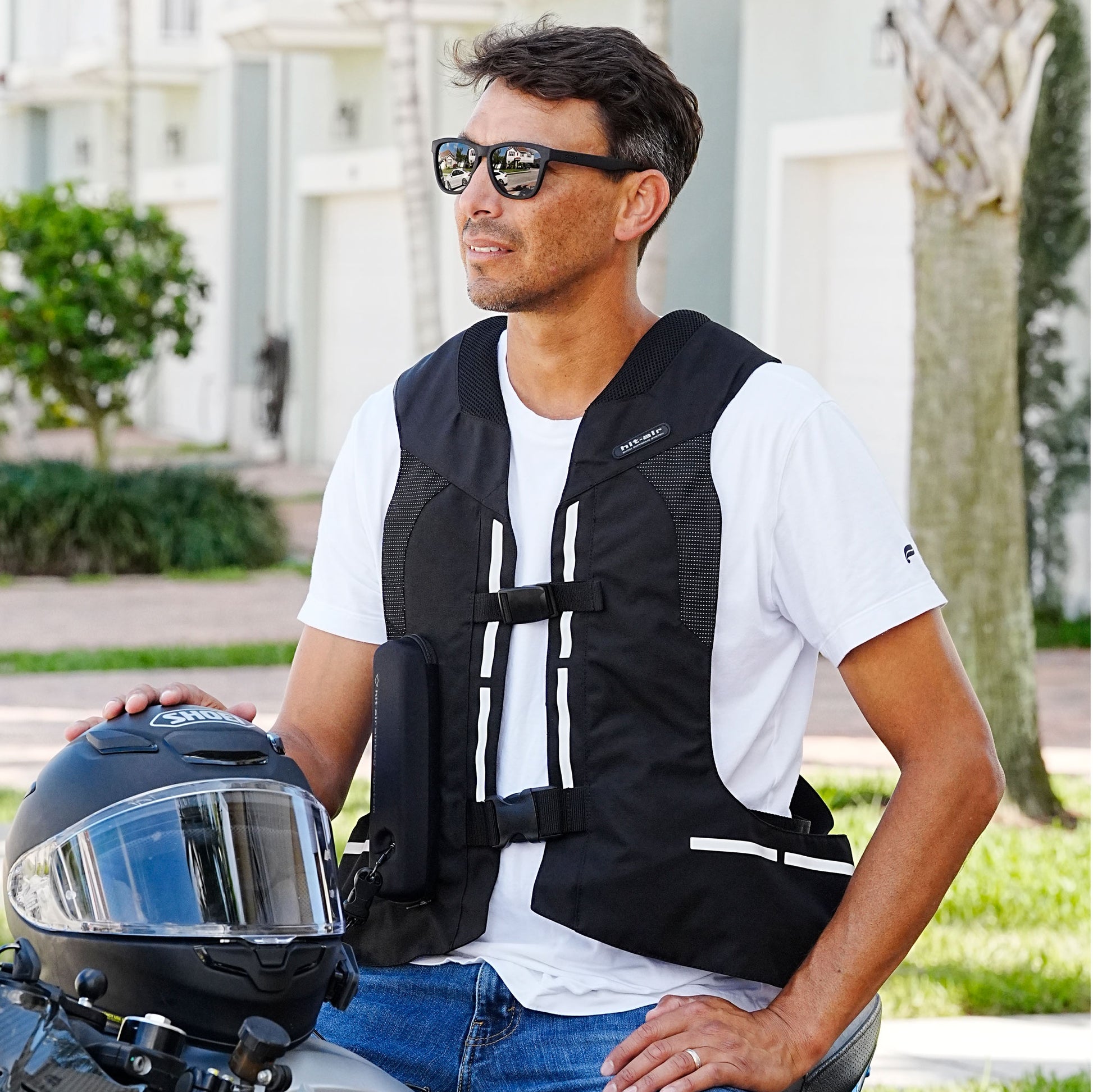 Man wearing a Hit-Air ST black motorcycle safety vest and sunglasses, holding a helmet.