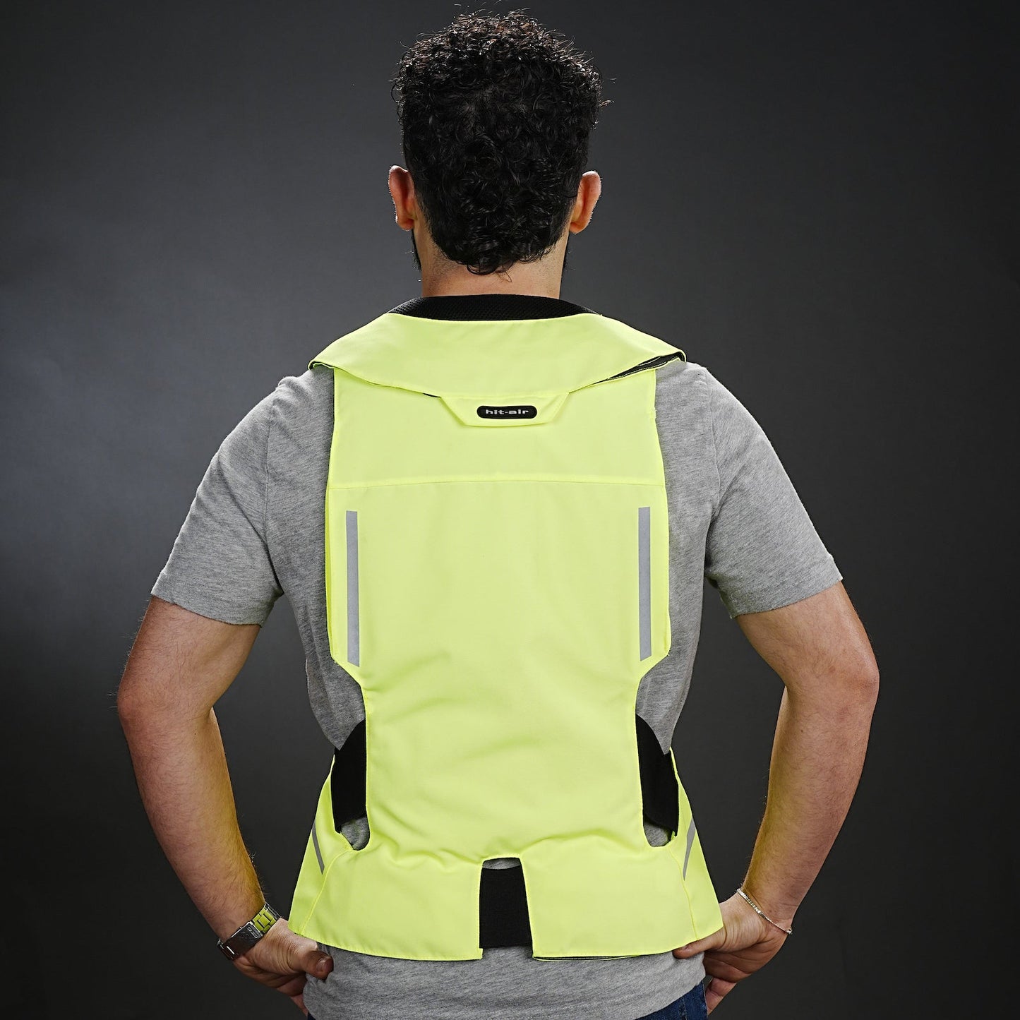 Person wearing a bright yellow ST Hit Air safety vest on a dark background