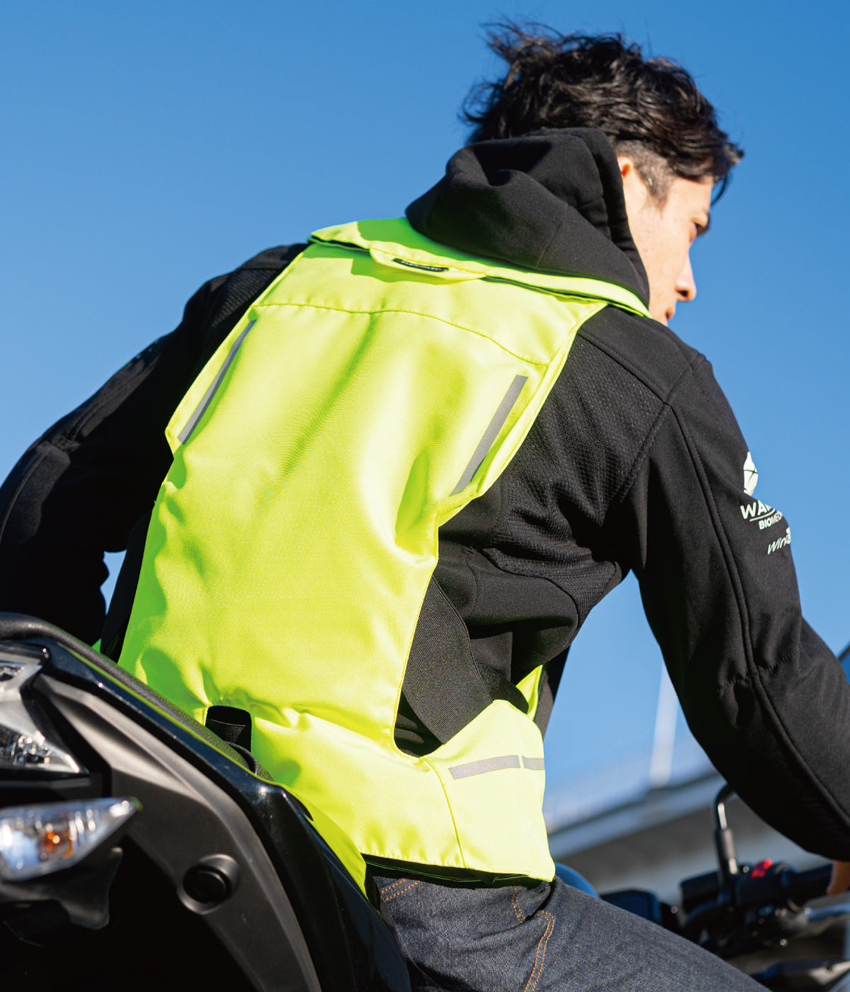 Person wearing a high-visibility vest on a motorcycle against a clear blue sky.